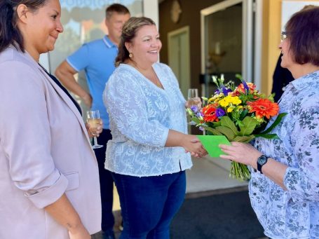 Martina mit der DEB Schulleitung Dorothe Lischke Eine Frau überreicht einer anderen Frau einen Blumenstrauß, während andere zuschauen.
